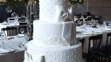 White wedding cake with lace and pearls decorated with bow ribbons between tiers.