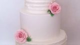 Three tiers wedding cake with ruffles and pink flowers on top and between tiears.
